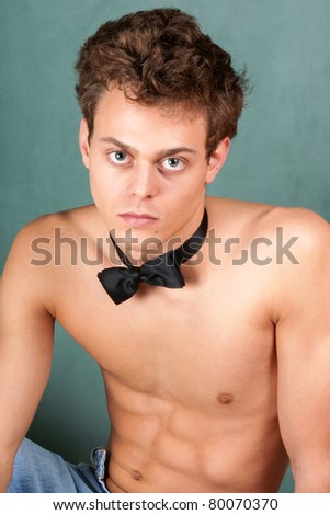 Sexy shirtless young man with jeans and bow tie over a green background