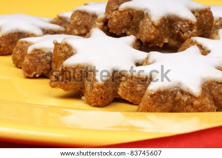 Close-up of some cinnamon star cookies (in german Zimtsterne), typical german and swiss Christmas cookies on a yellow plate over a red background.