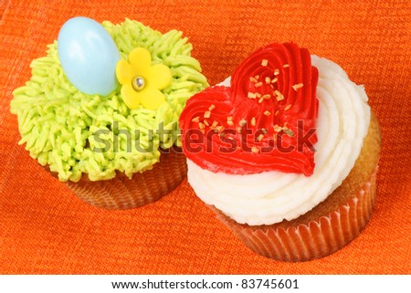 Two fancy holiday cupcakes over an orange background. A Valentine\'s day cupcake on the right and an Easter cupcake on the left.