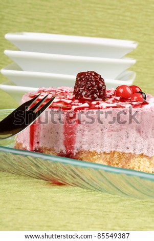 Wild berries bavarian cream on a transparent glass dish with dessert fork over a green background.