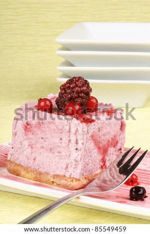 Wild berries bavarian cream on a white dish with dessert fork over a green background.