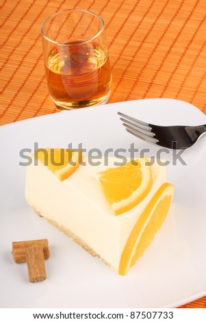 Slice of orange bavarian cream (bavarese) with dessert fork on a white porcelain dish and a glass of brandy
