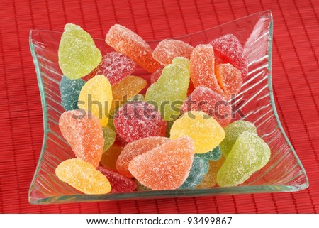 Assorted fruit shaped and flavored jellies in a transparent glass bowl over a red background