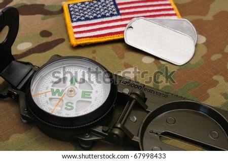 US military compass and US flag patch and dog tags on multicam camo background