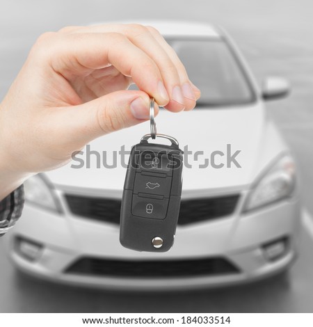 Male holding car keys with parked car on background - 1 to 1 ratio