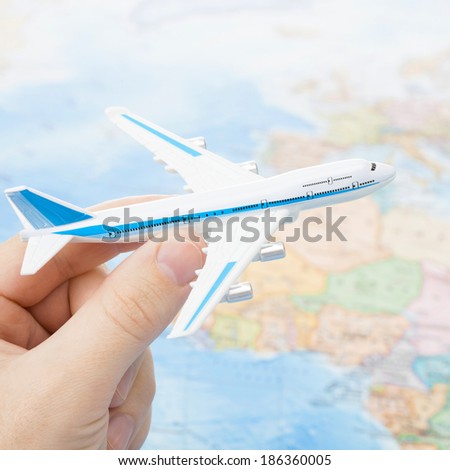 Toy aircarft in hand with world map on background with focus on the plane - 1 to 1 ratio