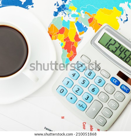 White coffee cup and calculator over world map and financial documents - view from top - 1 to 1 ratio