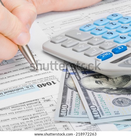 Male filling out 1040 US Tax Form with calculator and money on table - 1 to 1 ratio