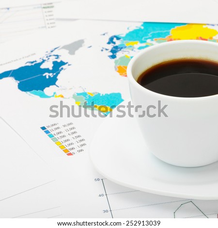 Coffee cup over world map and some financial documents next to it
