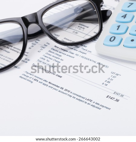 Calculator with pen, glasses and utility bill under it - close up shot