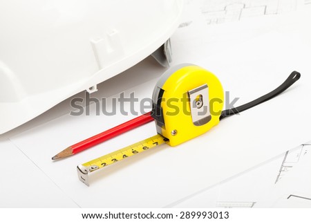 Yellow measure tape, red pencil and white construction helmet