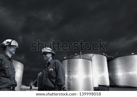 two refinery workers with large industrial fuel tanks