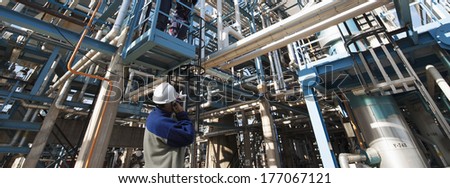 oil and gas worker pointing at large refinery construction, pipelines and pumps