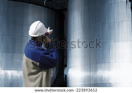 refinery worker in hard-hat pointing at industrial fuel and oil tanks