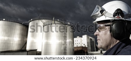 refinery worker with giant fuel storage tanks at sunset