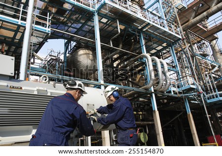 oil workers with machinery pumps inside large petroleum refinery