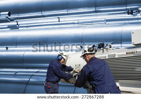 two oil workers with machinery, gas-pipes and pipelines in the background
