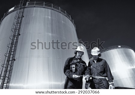 two oil workers with large fuel-tanks in background, slight blue toning concept