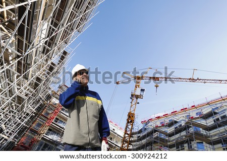 building worker talking in phone with a large construction site in background, super wide perspective