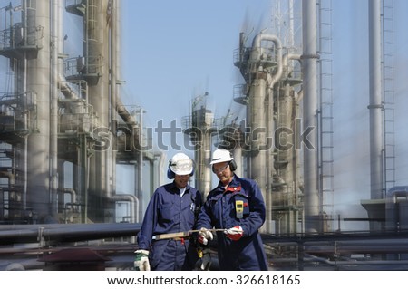 two power industry workers with refinery in the background, slight zoom effect