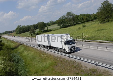 large clean truck driving on highway surrounded by spring-green countryside