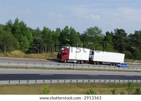 red/white truck speeding on highway surrounded by countryside