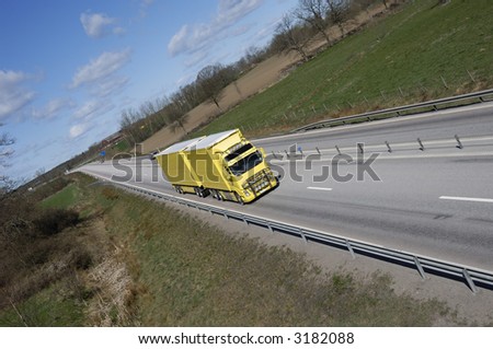 yellow truck driving on long straight of highway surrounded by country-side