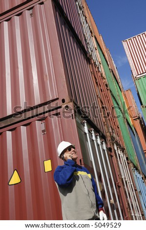 engineer talking in mobile-phone inside container port, stacks of containers in background