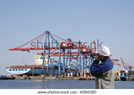 engineer, dock-worker, standing in front of commercial port with container-cranes and ship