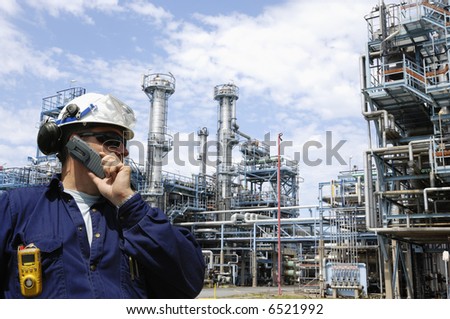 engineer talking in mobile-phone in front of large oil refinery, massive pipelines constructions