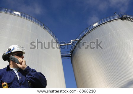 engineer talking in mobile-phone in front of refinery oil storage tanks