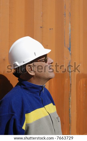 engineer in profile, wearing hard-hat, standing against colored  metal background