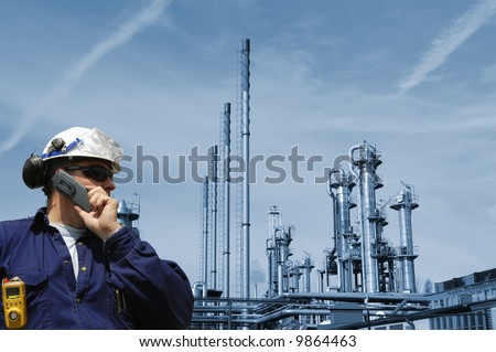 engineer talking in phone with a large blue toned oil and gas refinery in background