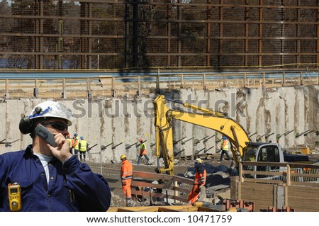 engineer in hard-hat supervising workers and bulldozers inside construction-site