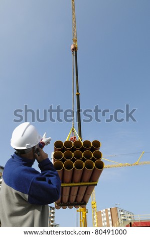 construction worker directing crane load of pipelines, building and construction industry
