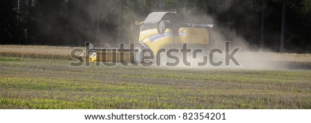 combine harvester in a wheat field, dust and smoke, trademarks removed