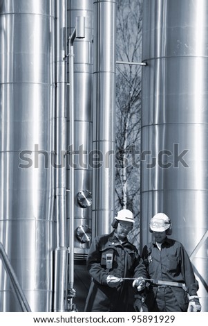 large shiny oil and gas pipes with two workers in foreground, blue toning concept