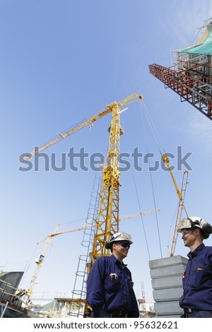 construction engineers, workers, giant cranes, scaffolding and machinery in background,