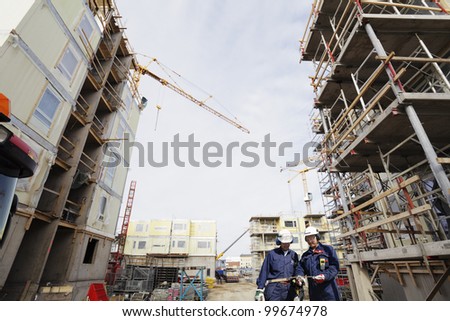 two construction workers inside large building-site, cranes and scaffoldings