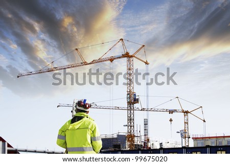 geodetist with measuring instruments, building-site in background, sunset shot