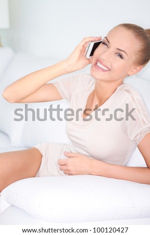 Happy woman sitting in an armchair laughing with friends over her mobile phone