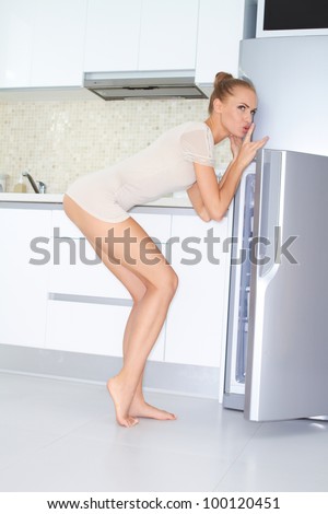Sexy woman in skimpy outfit looking back guiltily of her shoulder with a broad smile as she raids the fridge