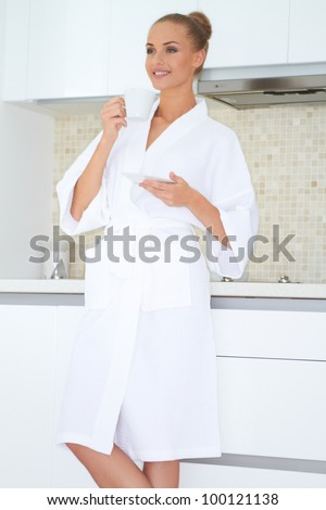 Smiling woman standing in a white bath robe enjoying a cup of coffee
