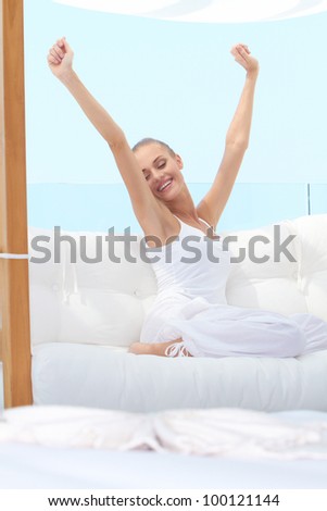 Pretty woman in casual outfit curled up on a white window seat stretching languidly in the warm sunshine