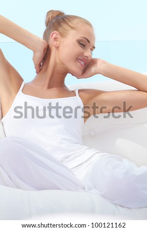Pretty woman in casual outfit curled up on a white window seat stretching languidly in the warm sunshine