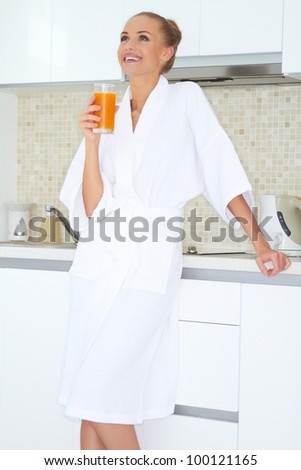 Glamorous woman in a white bath robe enjoying a large glass of fresh orange juice for breakfast