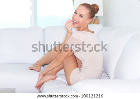 Woman sitting barefoot on a white sofa looking back over her shoulder