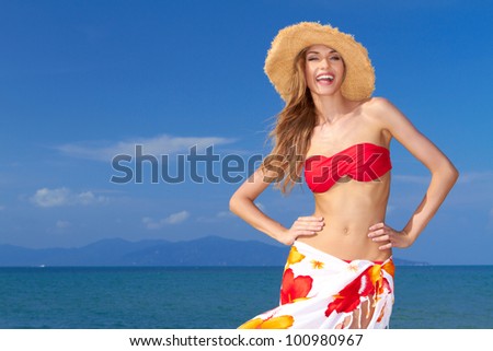 High-spirited beautiful woman laughing in merriment as she poses in front of the ocean in her bikini and colourful sarong