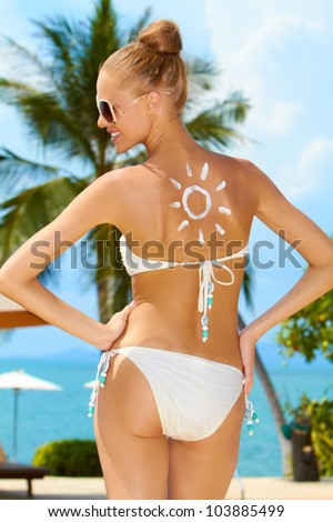 Attractive blonde woman in a bikini smiling at the sun painted on her back