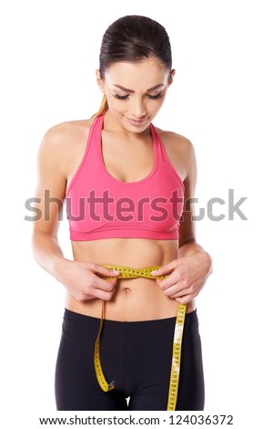 Young attractive slim female athlete measuring her waist with a tape meaure to check on her weightloss isolated on white
